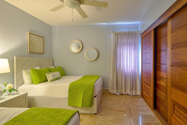 Une chambre d’hôtel avec un lit, un ventilateur de plafond, une table de chevet avec une lampe et une fenêtre avec des rideaux.