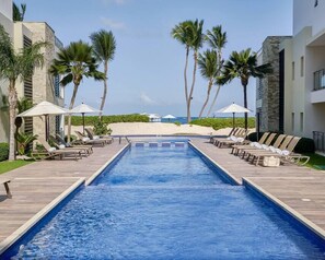 Une piscine avec des chaises longues et des parasols, des palmiers et une vue sur la plage.