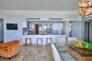 A modern kitchen with a central island, bar stools, and a dining table with a glass top.