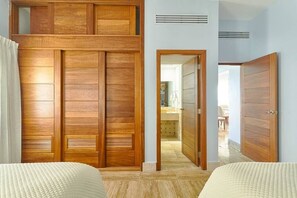 Une chambre avec un lit double, une armoire en bois et un couloir menant à la salle de bain.