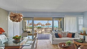 Ein modernes Wohnzimmer mit einem Glastisch, einer Couch mit bunten Kissen und Blick auf den Strand.