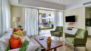 Un salon comprenant un canapé, une table basse et deux fauteuils, un téléviseur à écran plat et une vue sur l’extérieur.