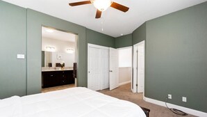 Une chambre avec un grand lit, un ventilateur de plafond et un dressing.