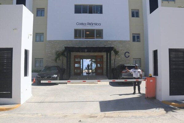 A building with a sign reading 'Costa Atlántica' and a gated entrance with a security guard. - Deluxe Beachfront Apartment with Pool and Sea View (Punta Cana)