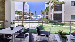 Un balcon avec coin salon extérieur, une piscine et une vue sur un immeuble bordé de palmiers.