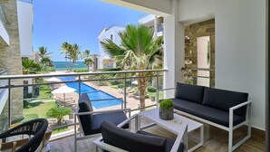 A balcony with a pool view, a sofa, and a table. - Deluxe Beachfront Apartment with Pool and Sea View (Punta Cana)