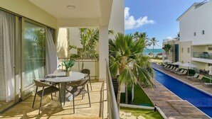 Un balcón con mesa y sillas, una piscina y vista a la playa.