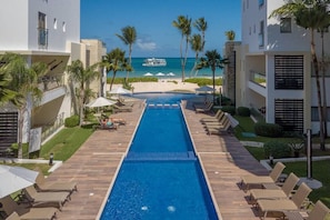 A swimming pool with lounge chairs and umbrellas, a beach view, and palm trees.