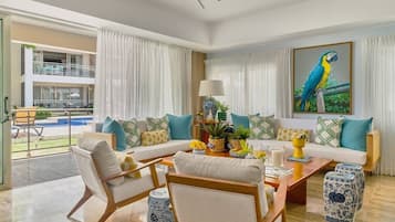 Una sala de estar moderna con un conjunto de sofá, una mesa de centro y sillas, un ventanal con cortinas y un cuadro de un loro.