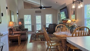 A spacious living room with a wooden floor, a ceiling fan, a dining area with a table and chairs, and a TV mounted on the wall. - Get Ready For Summer At Anglers Inn-1 mile from Pkwy (Pigeon Forge)