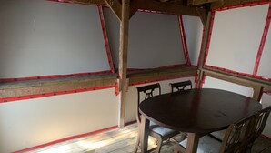 Une pièce avec une table en bois et quatre chaises, des poutres en bois au plafond et un mur blanc avec des moulures rouges.