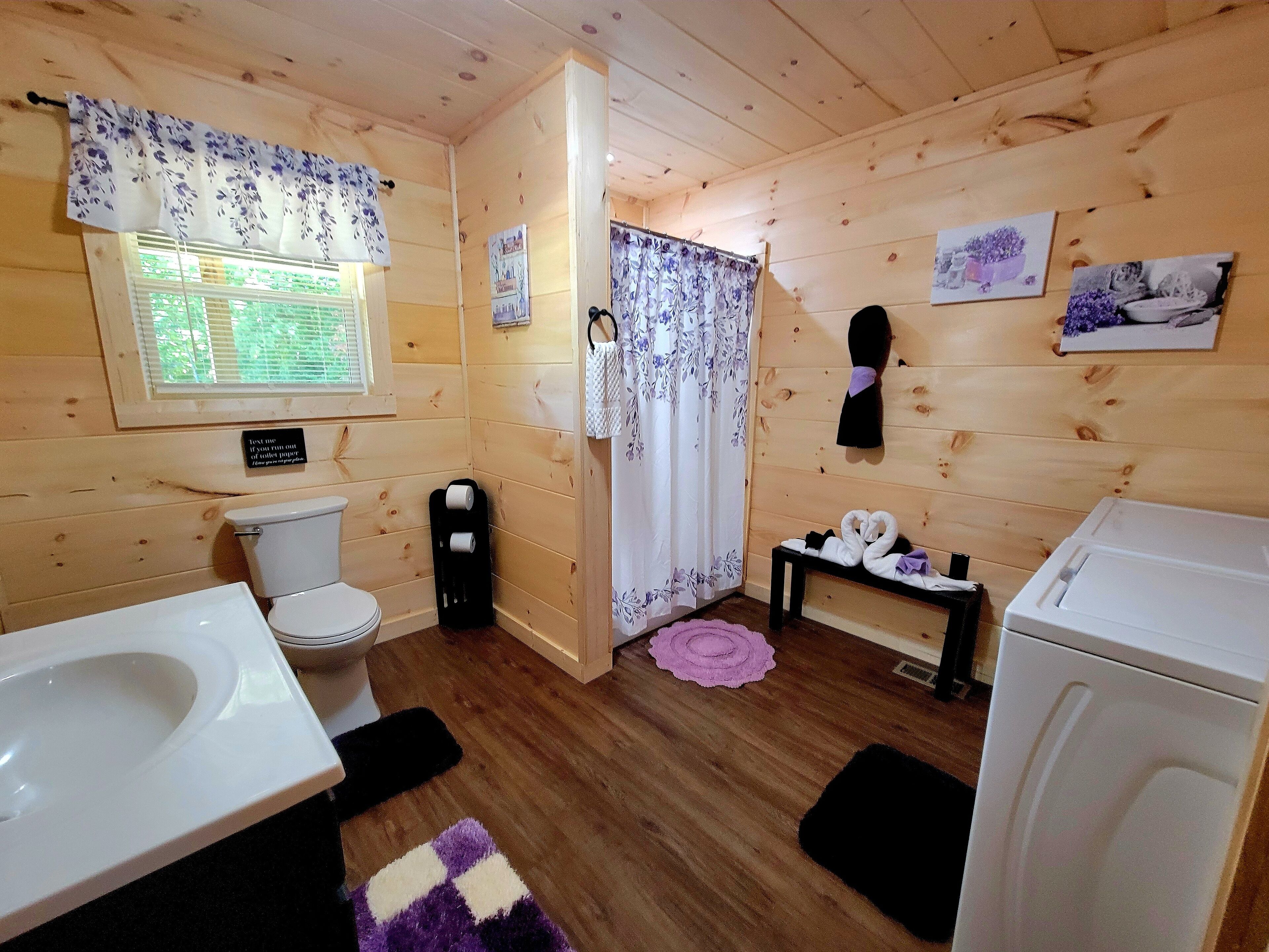 A wooden cabin bathroom with a toilet, sink, shower, and a small table with towels.