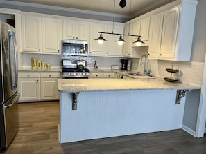 Een keuken met witte kasten, een roestvrijstalen koelkast, een dubbele oven, een magnetron en een spoelbak met twee bakken.