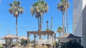 A courtyard with palm trees, a pergola, and a building with a white facade. - Beachfront condo with spectacular view (Corpus Christi)