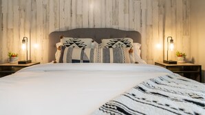 Een slaapkamer met een houten hoofdeinde, twee nachtkastjes met lampen, een bed met gestreepte kussens en een groot tapijt.