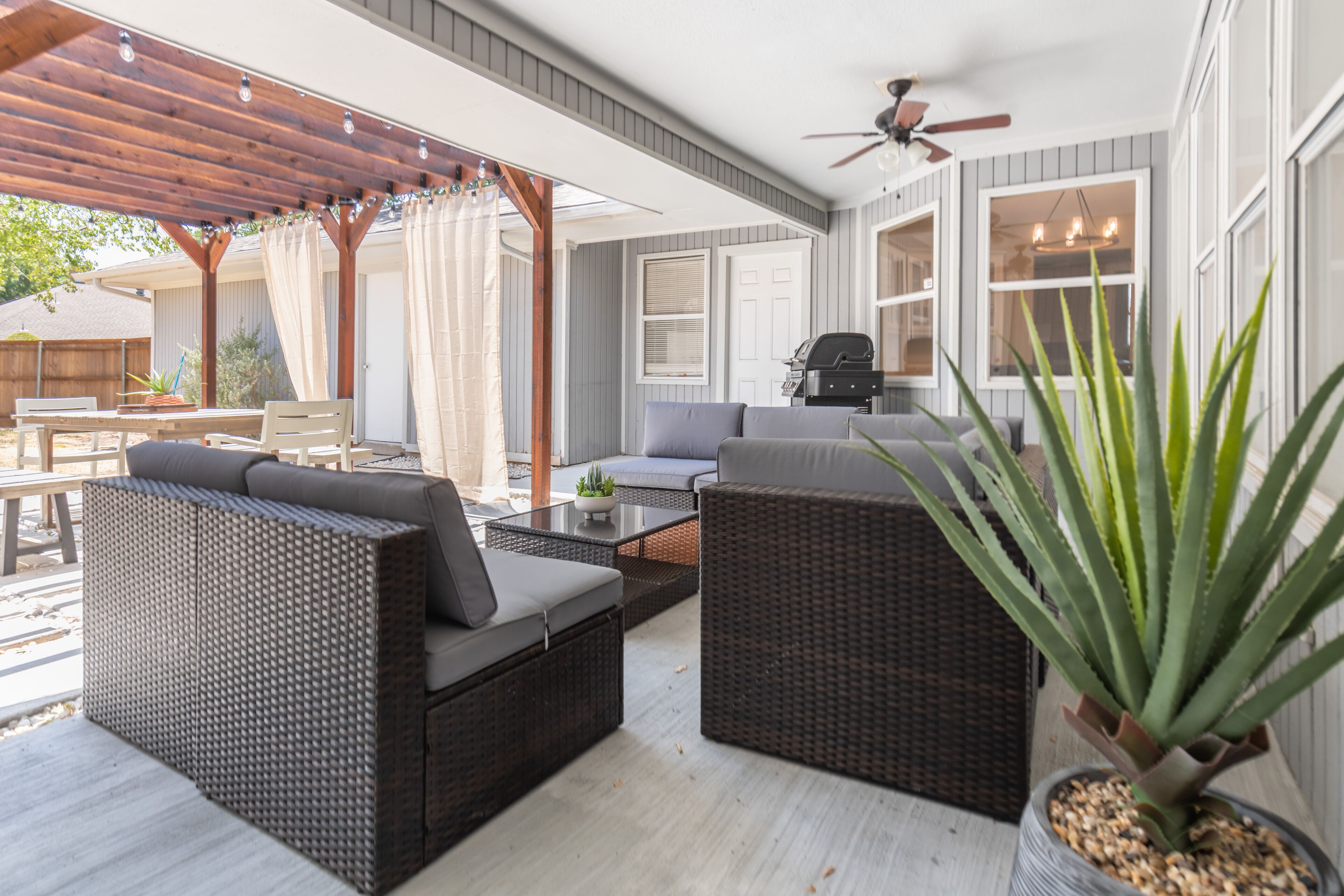 A covered patio area with wicker furniture, a ceiling fan, and a potted plant.