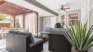 Een overdekt terras met rieten meubilair, een plafondventilator en een potplant.
