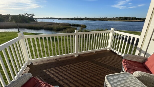 A wooden deck with white railings, a wicker chair, and a red cushion. - Boater’s Paradise (Crystal River)