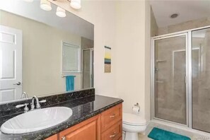 A bathroom with a white sink, wooden vanity, a large mirror, a toilet, and a glass shower enclosure. - Boater’s Paradise (Crystal River)