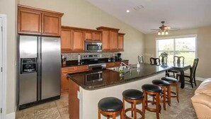 A kitchen with wooden cabinets, a stainless steel refrigerator, a microwave, and a large island with bar stools. - Boater’s Paradise (Crystal River)