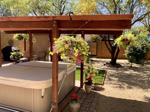 Een overdekt terras met een jacuzzi, omringd door potplanten en een betegeld terras.