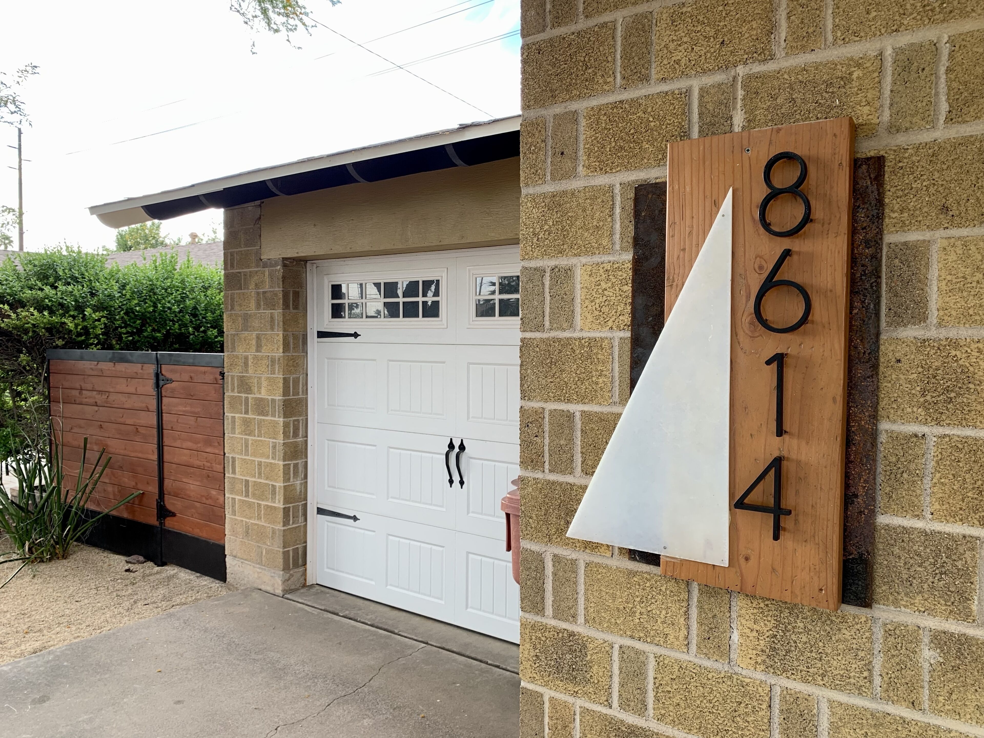 Une maison avec une porte de garage blanche, une boîte aux lettres en bois portant le numéro 8614 et un mur en briques.
