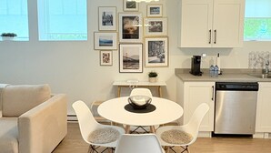 A modern kitchen with white cabinets, a stainless steel dishwasher, and a dining area with a round table and four chairs.