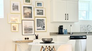 A modern kitchen with white cabinets, a dining table with chairs, and a wall adorned with framed photographs.