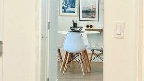 A hallway with a dining area, featuring a table with chairs, a hanging light fixture, and framed pictures on the wall.