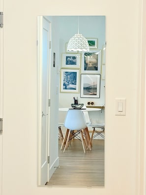 En gang med spiseområde, med et bord med stole, en hængende lampe og billeder i rammer på væggen.