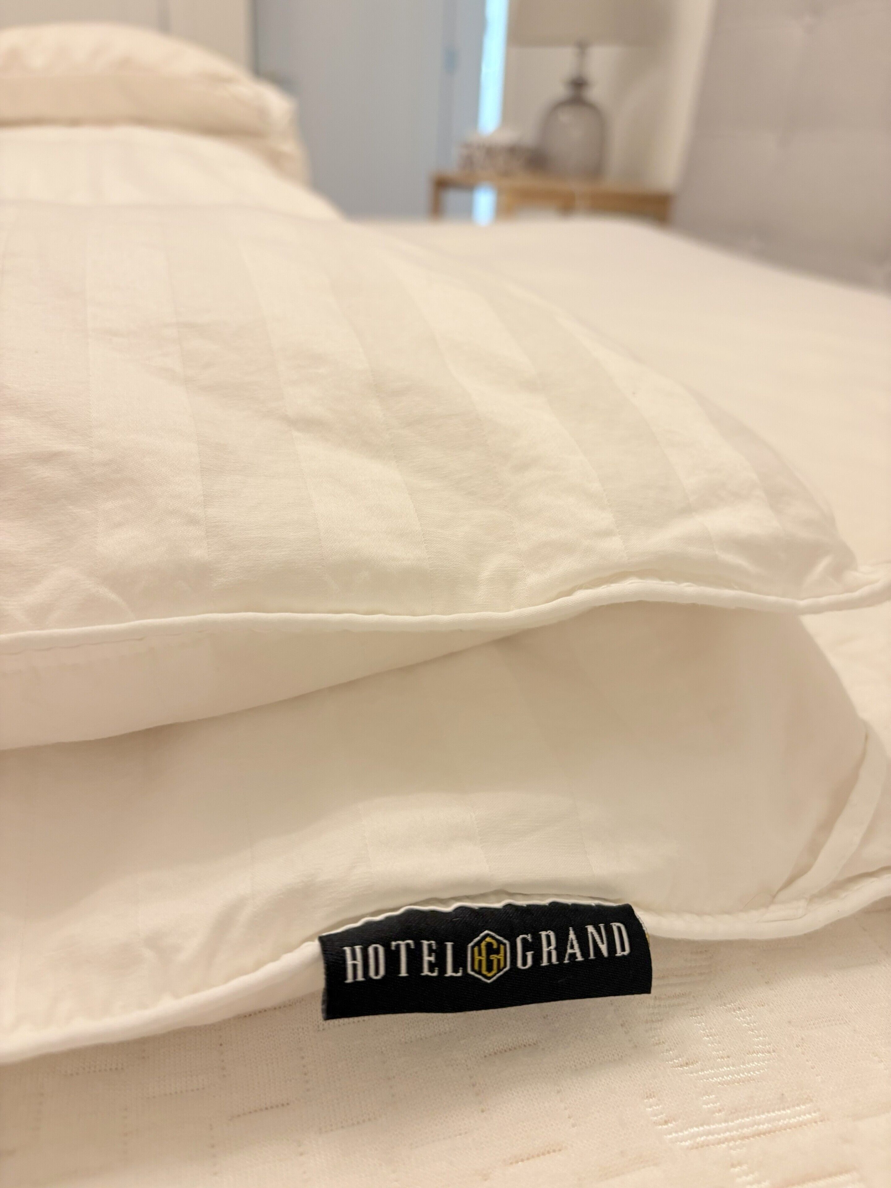 A bed with a pillow and a black tag labeled 'HOTELGRAND'.