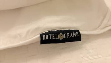 En säng med en kudde och en svart etikett med texten ”HOTELGRAND”.