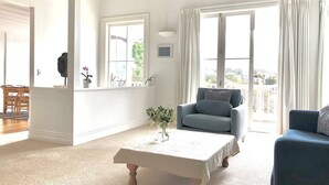 Ein geräumiges Wohnzimmer mit großem Fenster, einem grauen Sofa, einem blauen Sessel und einem Holztisch.