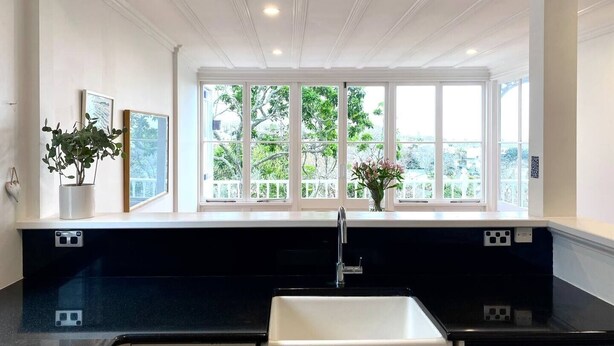 Eine moderne Küche mit großem Fenster, schwarzer Arbeitsplatte und weißem Spülbecken.