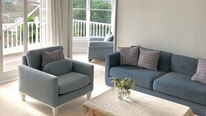 Ein geräumiges Wohnzimmer mit großem Fenster, einem blauen Sofa, einem grauen Sessel und einem Holztisch.