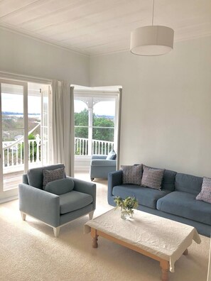 Ein geräumiges Wohnzimmer mit großem Fenster, einem blauen Sofa, einem grauen Sessel und einem Holztisch.