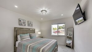 A bedroom with a bed, a ceiling light, a window, and a TV mounted on the wall.