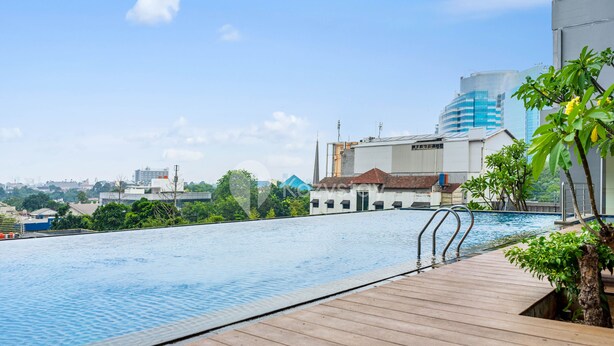 Una piscina en la azotea con un deck de madera, rodeada de edificios y vegetación.
