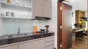 Una cocina moderna con estufa integrada, un lavamanos y una puerta de madera que da a una sala de estar con un escritorio y un televisor.