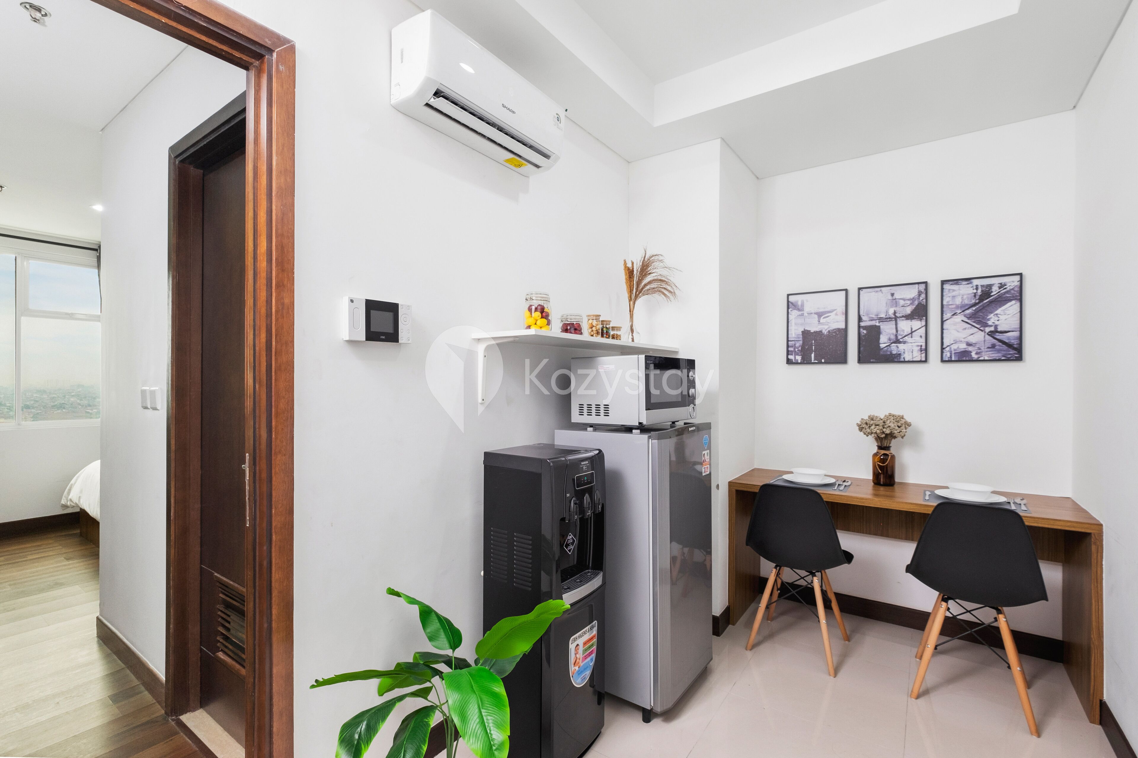 Een moderne keuken met een koelkast, magnetron en waterdispenser. Er is een houten bureau met twee stoelen en een klein tafeltje met een bloevas.
