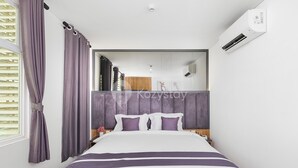 Una habitación de hotel moderna con una cama grande, cabecero, unidad de aire acondicionado y reflejo de la habitación en un espejo.