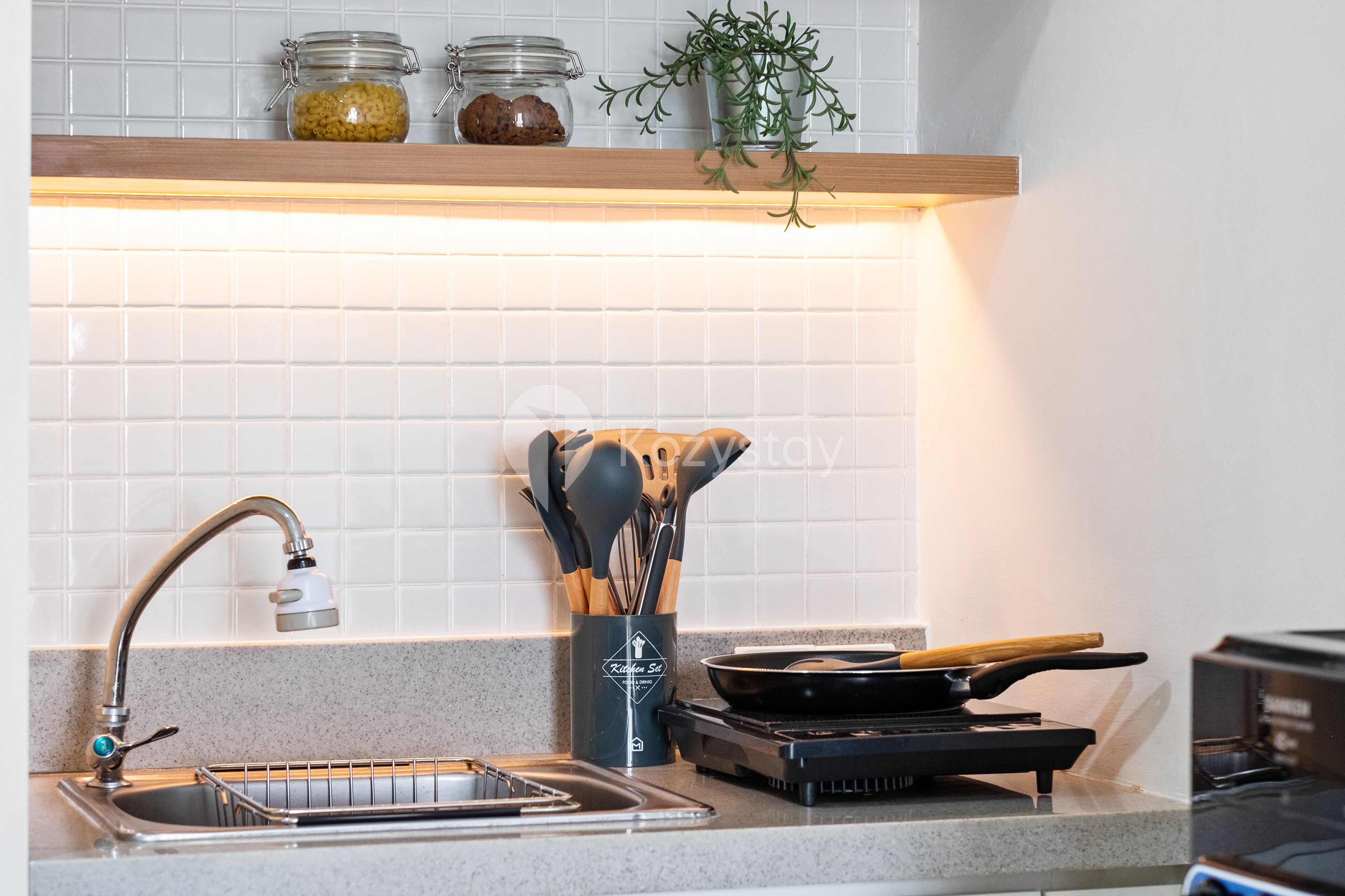 A kitchen with a stainless steel sink, a stove, and a utensil holder.