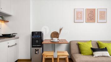 Una cocina compacta con refrigerador, una mesita con un tazón y un florero, y un sofá con cojines verdes.