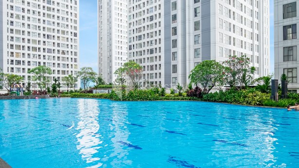 Piscina com água azul cristalina, rodeada por vegetação e edifícios residenciais altos.
