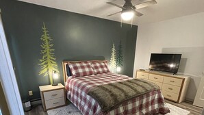 Quarto com cama, ventoinha no teto, televisão e cómoda.