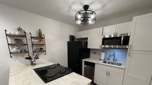 Cozinha compacta com armários brancos, geladeira preta, micro-ondas de aço inoxidável e fogão por indução preto.