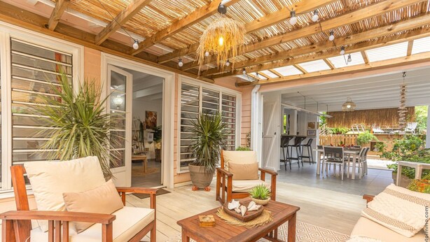 An open-plan living area with wooden furniture, potted plants, and a dining area visible through an open door. - Villa Mahana Martinique (Les Trois-Îlets)