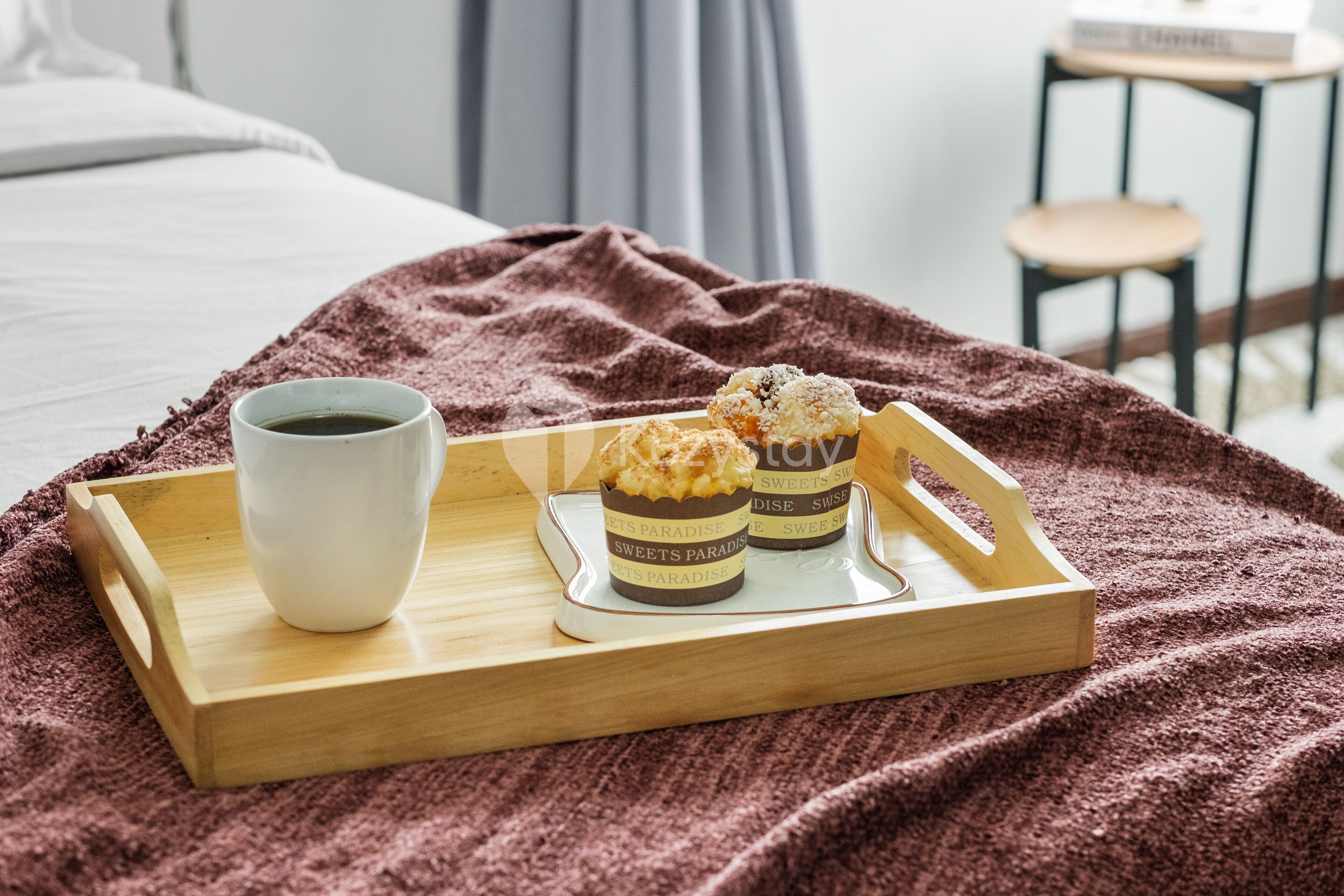 Una bandeja con una taza de café y tres cupcakes sobre una cama con una manta marrón.