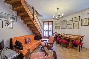 A cozy living room with a wooden staircase, a dining area with a wooden table and chairs, and a computer desk.