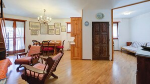 A spacious living room with a wooden floor, a dining area with a table and chairs, a chandelier, and a large wooden door. - Il Rododendro  (City Center) (Bardonecchia)